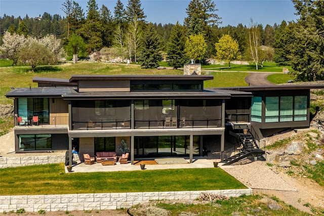 rear view of property featuring a patio, outdoor lounge area, a lawn, stairway, and a chimney