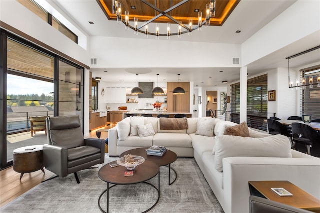 living room with a chandelier, light wood-style floors, and a towering ceiling