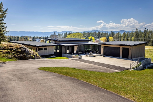 modern home with driveway, a mountain view, a front yard, a garage, and metal roof