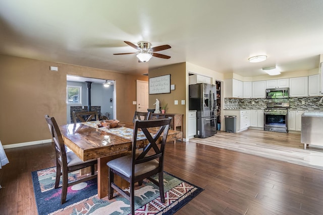 dining room with a wood stove, ceiling fan, wood finished floors, and baseboards