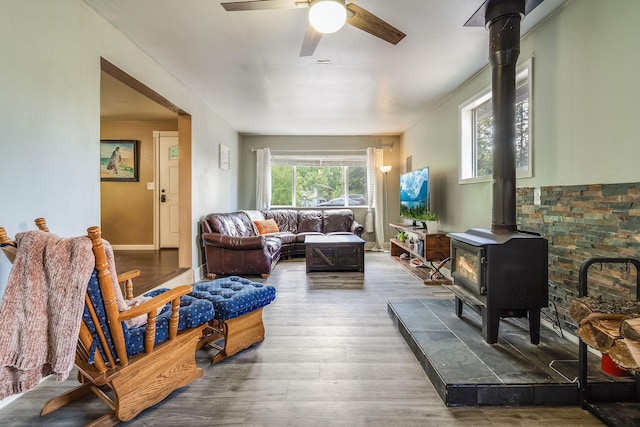 living room featuring a wood stove, ceiling fan, and wood finished floors