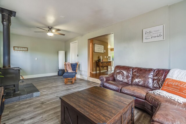 living area featuring a wood stove, ceiling fan, wood finished floors, and baseboards