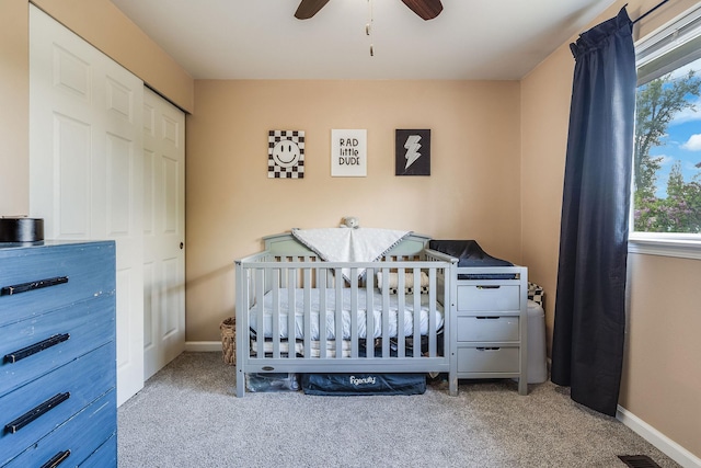 carpeted bedroom with baseboards, ceiling fan, a nursery area, and a closet