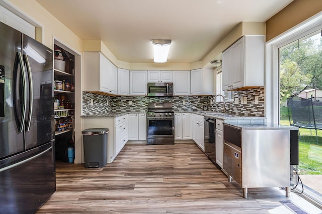 kitchen featuring appliances with stainless steel finishes, a sink, light stone counters, and wood finished floors