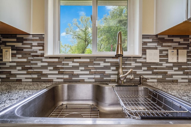 kitchen view of a sink, white cabinets, and decorative backsplash