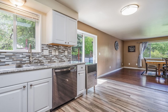 kitchen with stainless steel dishwasher, a sink, white cabinetry, light wood-style flooring, and decorative backsplash