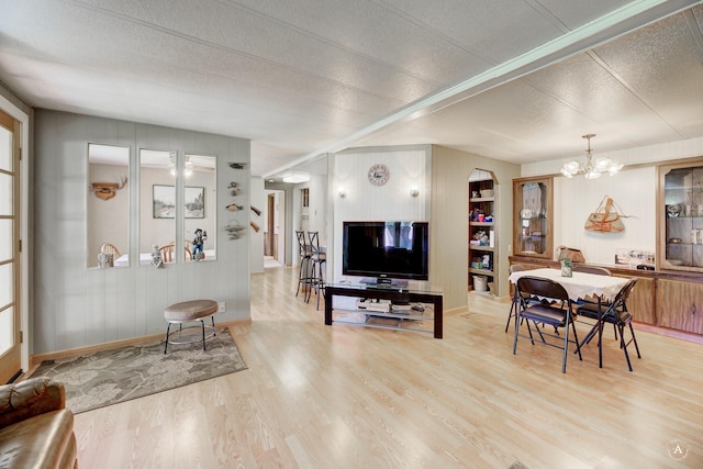 living room featuring a chandelier, wood finished floors, a textured ceiling, baseboards, and wood walls
