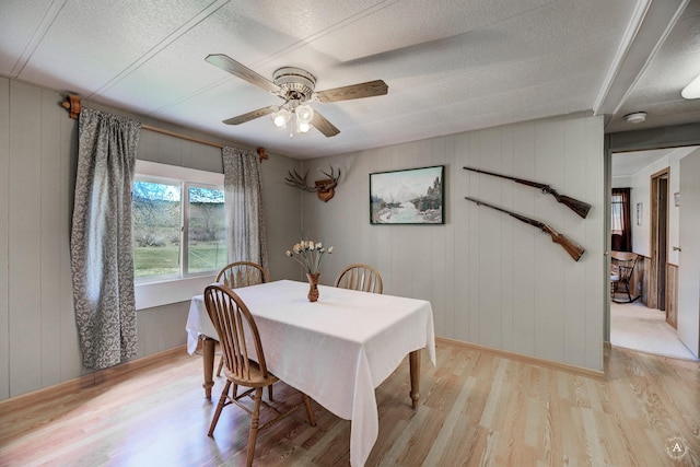dining area featuring light wood-style floors, ceiling fan, a textured ceiling, and baseboards