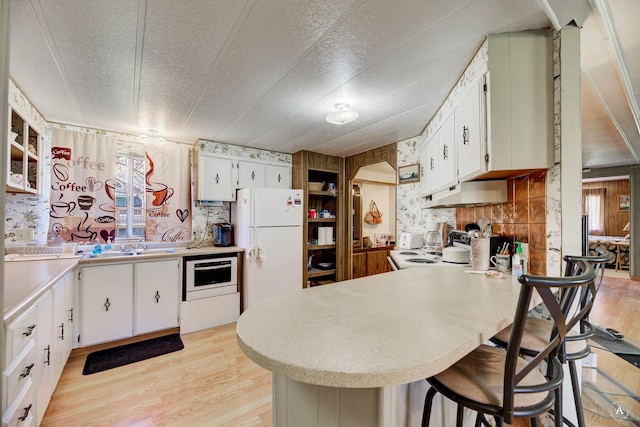 kitchen with white appliances, under cabinet range hood, a peninsula, light wood-style flooring, and a textured ceiling