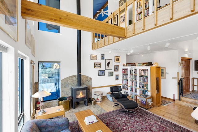 living room with a wood stove, wood finished floors, track lighting, baseboards, and a high ceiling