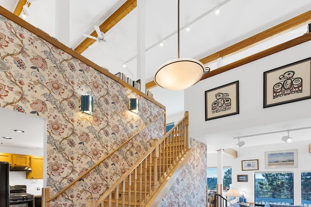 staircase with rail lighting, a ceiling fan, and a towering ceiling