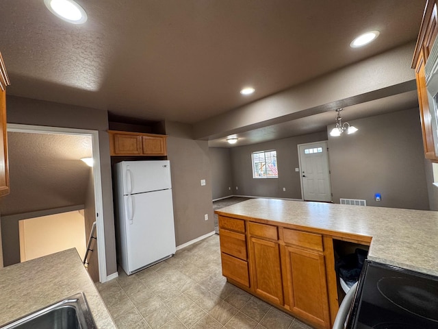 kitchen featuring freestanding refrigerator, light countertops, a sink, brown cabinets, and baseboards