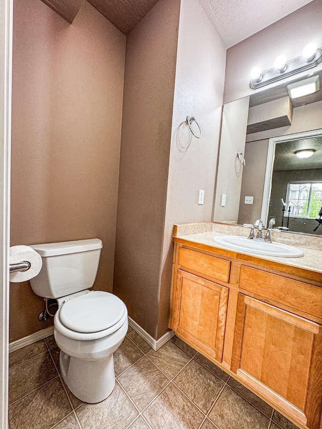 bathroom with toilet, vanity, tile patterned floors, baseboards, and a textured ceiling