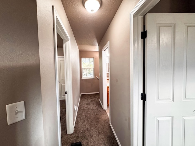 hall featuring a textured ceiling, carpet floors, and baseboards