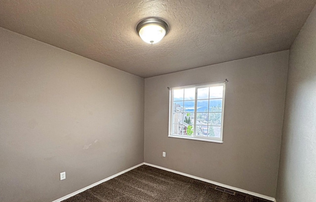 spare room with dark carpet, baseboards, and a textured ceiling
