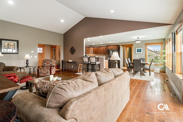 living area with light wood finished floors, recessed lighting, high vaulted ceiling, and baseboards