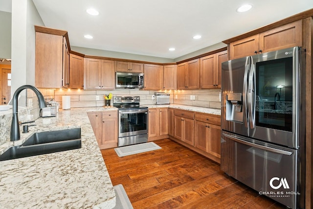 kitchen with stainless steel appliances, a sink, dark wood-type flooring, backsplash, and light stone countertops