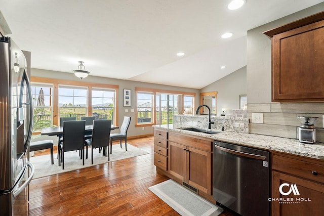 kitchen featuring appliances with stainless steel finishes, a sink, backsplash, a peninsula, and hardwood / wood-style flooring
