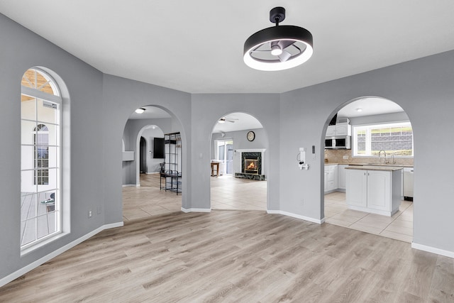 2965 Terrace Dr, Missoula, MT 59803 - unfurnished living room featuring light wood-style floors, a warm lit fireplace, arched walkways, and baseboards
