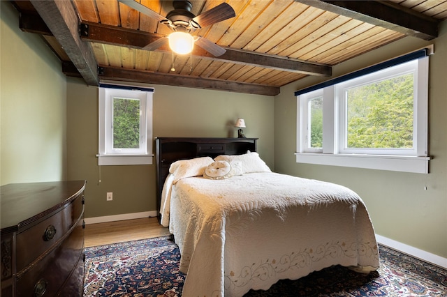 bedroom featuring wooden ceiling, beam ceiling, multiple windows, baseboards, and light wood finished floors