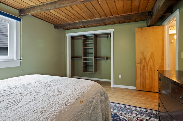 bedroom featuring wood finished floors, beamed ceiling, wooden ceiling, a closet, and baseboards