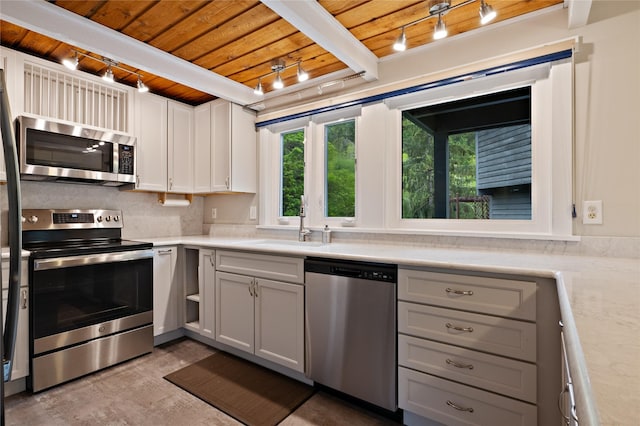 kitchen featuring stainless steel appliances, wood ceiling, a sink, light countertops, and track lighting