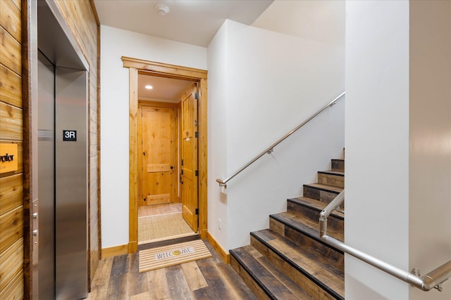 stairway with elevator, wood finished floors, baseboards, and recessed lighting