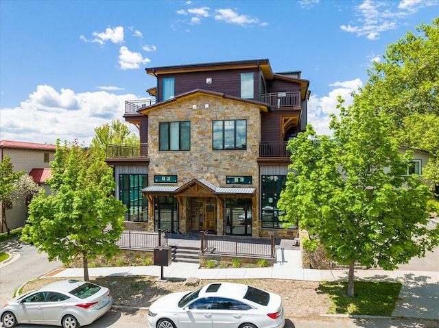 view of front of house with stone siding, a balcony, a porch, and uncovered parking