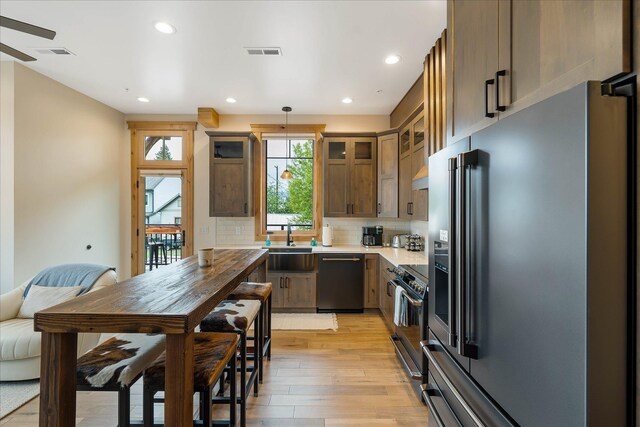 kitchen featuring appliances with stainless steel finishes, light wood-style floors, backsplash, recessed lighting, and glass insert cabinets