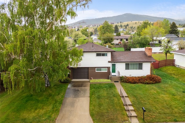 split level home featuring concrete driveway, a mountain view, a garage, and a chimney