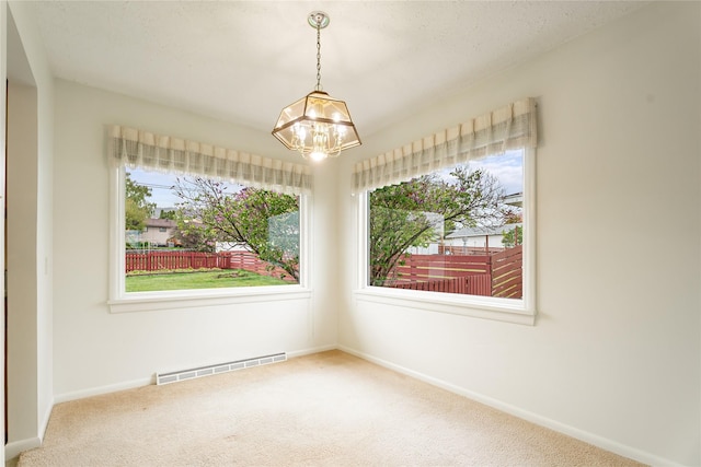 spare room featuring carpet, a chandelier, healthy amount of natural light, and baseboards