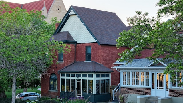 rear view of house featuring a sunroom, roof with shingles, entry steps, and brick siding