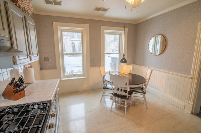 dining room with light wood-type flooring, a wainscoted wall, crown molding, and ceiling fan