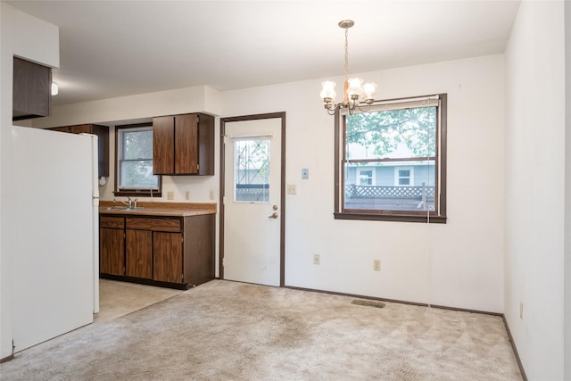 kitchen with freestanding refrigerator, a sink, a chandelier, light carpet, and hanging light fixtures