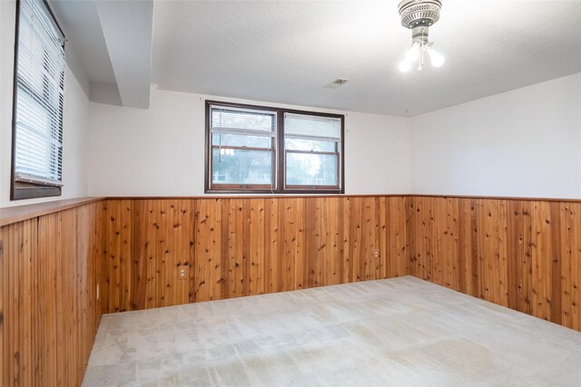 unfurnished room featuring healthy amount of natural light, wainscoting, wooden walls, and carpet
