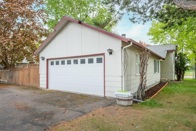 view of side of home featuring a garage, a shingled roof, and fence