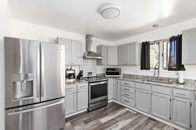 kitchen with appliances with stainless steel finishes, wall chimney exhaust hood, a sink, gray cabinets, and light stone countertops