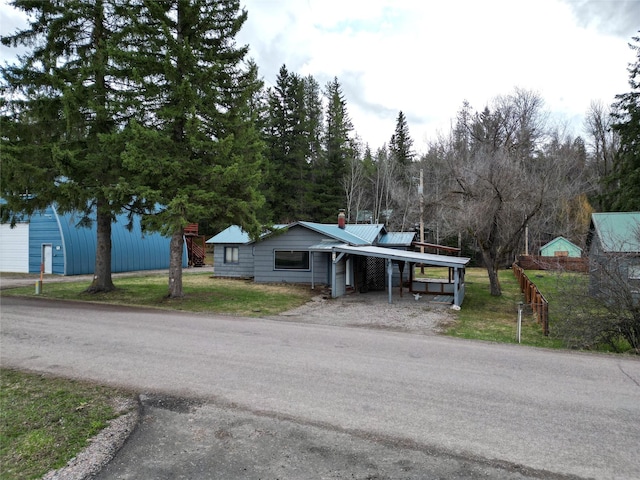 view of front facade featuring driveway, a carport, metal roof, a front lawn, and a chimney