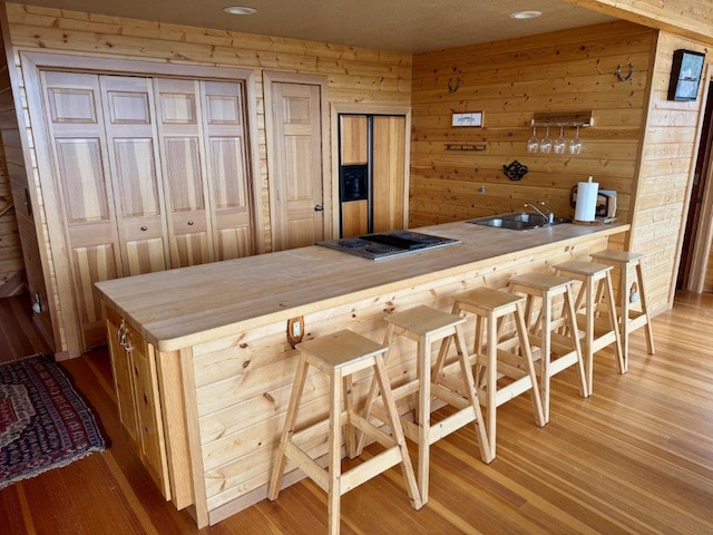 bar area with stainless steel stovetop, a sink, light wood finished floors, wood walls, and recessed lighting