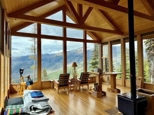 sunroom with wood finished floors, wood ceiling, a deck with mountain view, and a wood stove