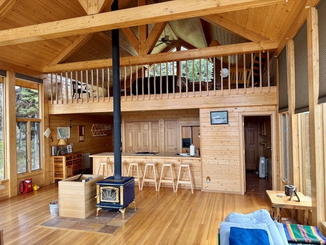 living room featuring a wood stove, wooden walls, high vaulted ceiling, wood finished floors, and ceiling fan