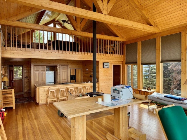dining space with high vaulted ceiling, a wood stove, wood walls, beamed ceiling, and wood-type flooring