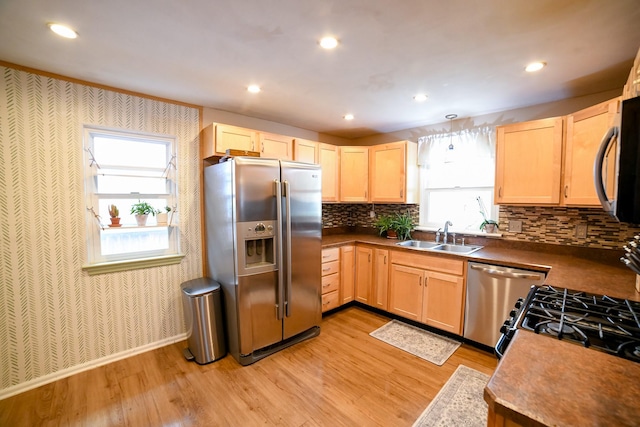 kitchen featuring appliances with stainless steel finishes, light brown cabinetry, a sink, light wood-style flooring, and wallpapered walls