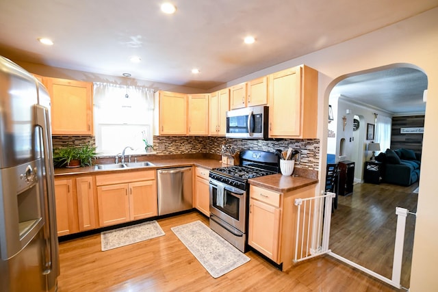 kitchen with appliances with stainless steel finishes, light brown cabinetry, a sink, arched walkways, and recessed lighting