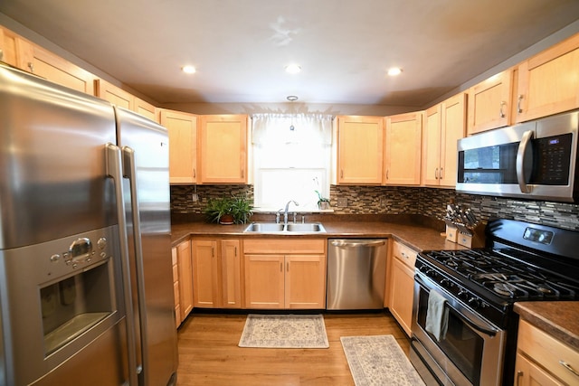 kitchen with appliances with stainless steel finishes, a sink, light brown cabinetry, dark countertops, and recessed lighting