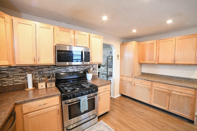 kitchen with appliances with stainless steel finishes, light brown cabinets, arched walkways, light wood-style floors, and recessed lighting