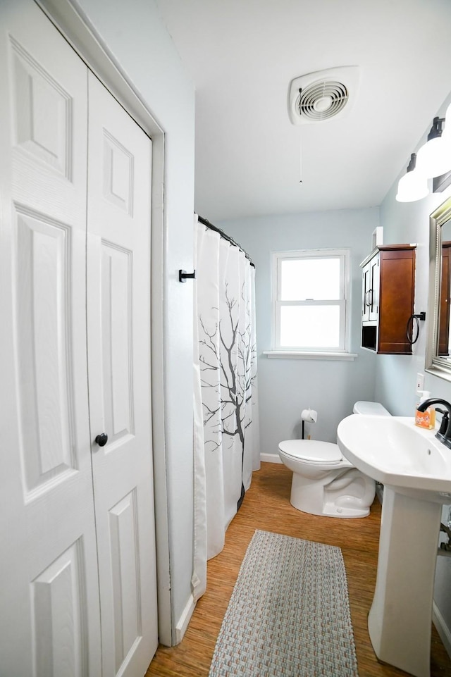 bathroom featuring toilet, wood finished floors, baseboards, and a shower with curtain