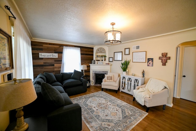 living room featuring arched walkways, a fireplace, a textured ceiling, wood finished floors, and wood walls