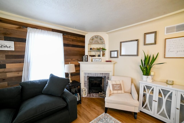 living room featuring wood walls, wood finished floors, a fireplace, and a textured ceiling