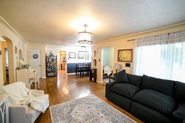 living area with arched walkways, wood finished floors, a textured ceiling, and ornamental molding